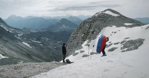 Man standing at the edge of skiing path, woman takes the slovenian flag Stock Footage 231092678