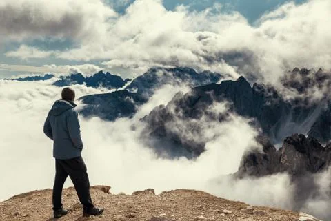 Man standing on the edge of view point with Dolomite Alps covered with clouds Stock Photos