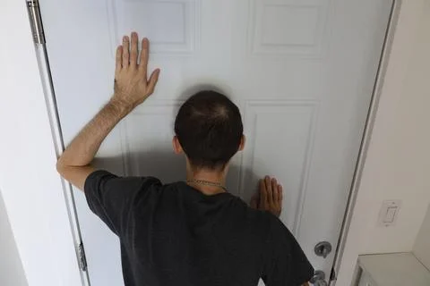 Man standing facing door with hands on surface indoor tension concept Stockfoto's
