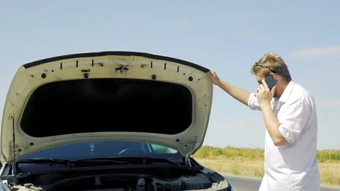 A man is standing in front of a car with its hood open, talking on his phone Stock Footage 319826739