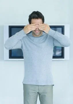 Man standing in front of widescreen TV on wall, hands covering eyes Stock Photos