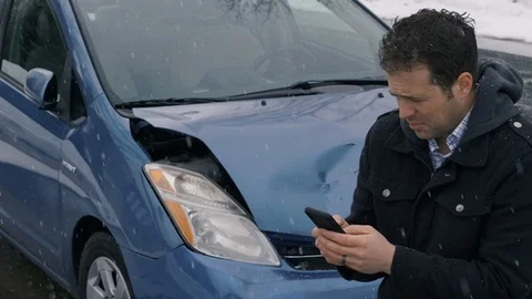 Man standing in front of wrecked car in the snow making phone call Video stock 104265909