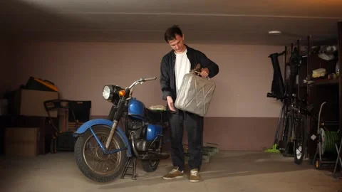 Man standing in a garage, holding a classic jerrycan while looking at a vintage Stock Footage 340352039