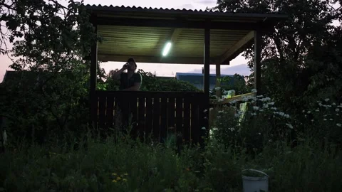 A man is standing in a gazebo. drinks a drink from a can. on a country plot. the Stock Footage 167694052