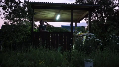 A man is standing in a gazebo. he drinks beer from a can. on a country plot. the Stock Footage 168899218
