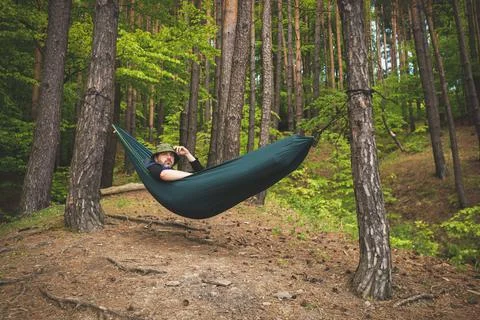 Man standing in a hammock on the edge of a forest admiring the landscape Stock Photos