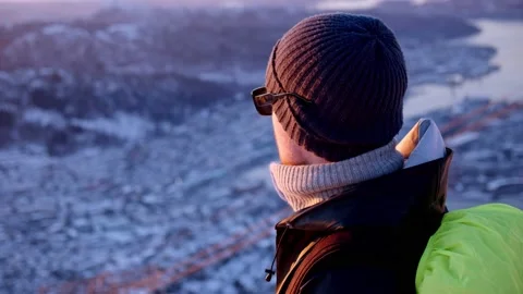 A man standing high up on a mountain looking out over a city during winter Stock Footage 233900496