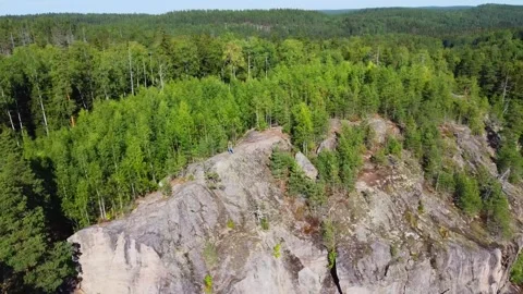 Man standing on high rock, mountain surrounded by forest and lake. Stock Footage 303660689