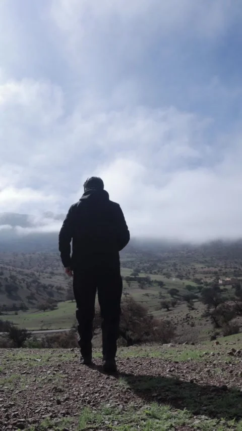 Man Standing on Hilltop Overlooking Misty Green Valley in Tiznit Morocco 動画素材 332776658