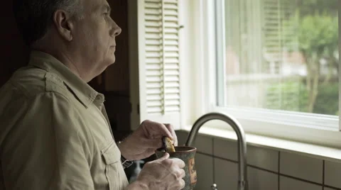 Man standing in his kitchen drinking coffee and eating a biscotti 4k Video stock 63318181