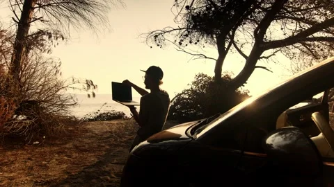 Man Standing Holding Laptop in Hands by Car at Sunset Near the Sea 動画素材 341939748
