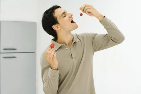 Man standing in kitchen, eating berries Фото