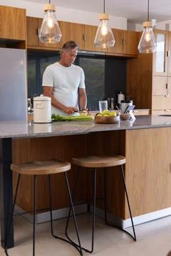 Man standing at kitchen island, preparing vegetables on cutting board with Stock Photos