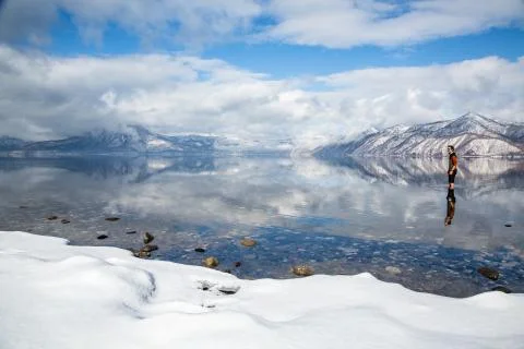 Man standing knee deep in shallow, calm water in very cold alpine lake surrou Stock Photos