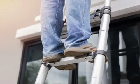 Man standing on ladder, low angle view, man climbing ladder against outdoors. Stock Photos