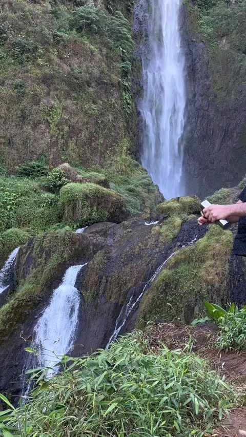 Man Standing by Large Waterfall in Tropical Forest Vertical Shot Video stock 323907395