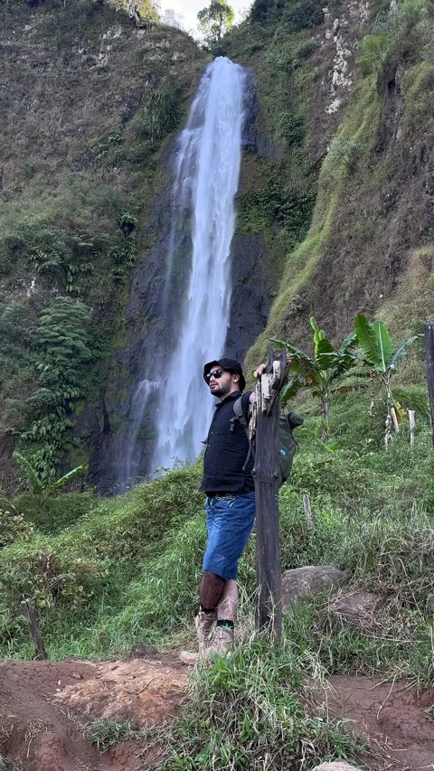 Man Standing by Large Waterfall in Tropical Forest Vertical Medium Shot Stock Footage 323910822