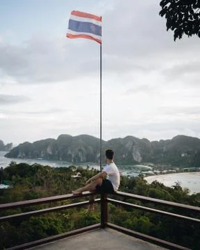 Man standing on ledge looking at beautiful Thailand island with Thai Flag wav Foto stock