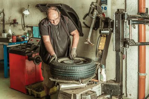 Man standing in a mechanic workshop while repairing a wheel Stock Photos