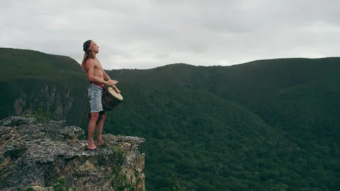 Man standing on a mountain and playing Djembe drums Stock Footage 279025879