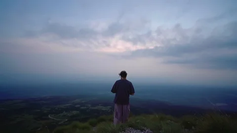 Man standing on a mountain overlooking endless fields on an dramatic cloudy Stock Footage 121805912