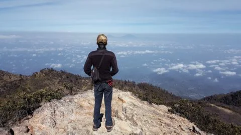 Man standing on a mountain peak looking out over a vast landscape of clouds Stock Photos
