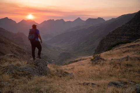 Man standing on a mountain summit looking to the red sunset Stock Photos