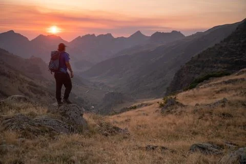 Man standing on a mountain summit looking to the red sunset Foto stock