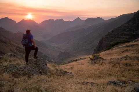 Man standing on a mountain summit looking to the red sunset Stock Photos