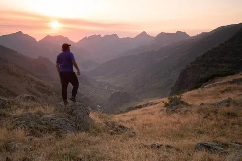 Man standing on a mountain summit looking to the red sunset Stock Photos
