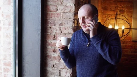 Man standing near a window in a cafe and drink coffee or tea, breakfast in Stock Footage 73127375