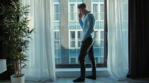 Man standing near a window in a modern house using smartphone. 動画素材 86237472