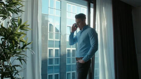 Man standing near a window in a modern house or office using smartphone. Stock Footage 86237474