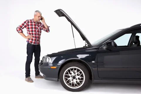 A man standing next to a broke down car while using a cell phone Stock Photos