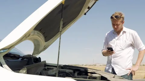 Man is standing next to a broken-down car with its hood up,looking at his phone Stock Footage 319825160