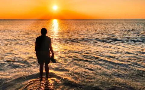 Man standing in ocean waves watching colorful sunset over the sea horizon Foto stock
