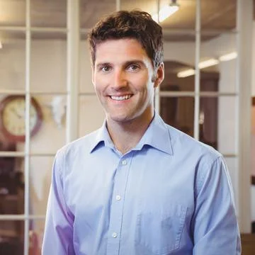 Man standing in office in front of white framed glass partition, with clock and Stock Photos