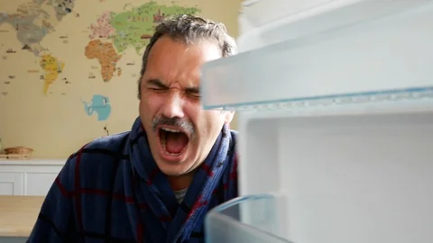 Man standing by an open fridge looking upset and hungry Stock Footage 127292134