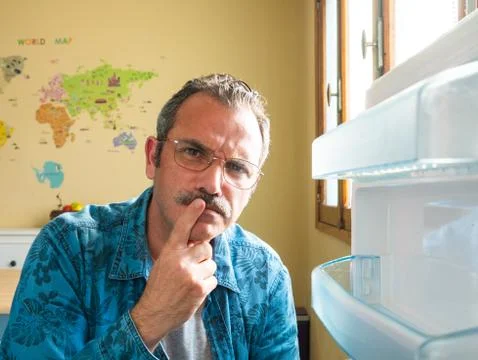 Man standing by an open fridge looking thoughtful Foto stock