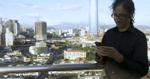 Man standing outside on a rooftop sending messages on his smart phone Stock Footage 86713249