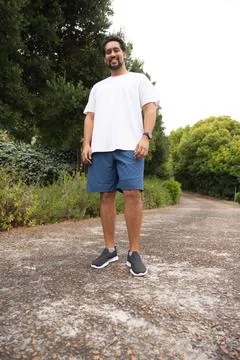 Man standing on pebble path in park, wearing white T-shirt and blue shorts, Stock Photos