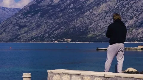 A man standing on a pier throwing stones into the sea Stock Footage 237998896