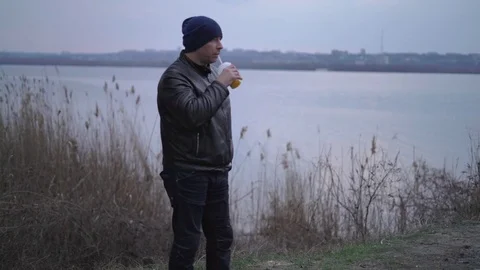 The Man Standing at the River Drinks the Juice, Looks in Front of Him, he is Stock Footage 73904377