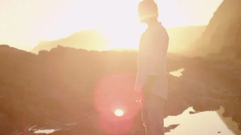 Man standing on the rocks and looking in the distance while the sun is settin Stock Footage 279791985