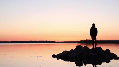 Man standing on rocks out on a lake at sunset Stock Footage 233209779