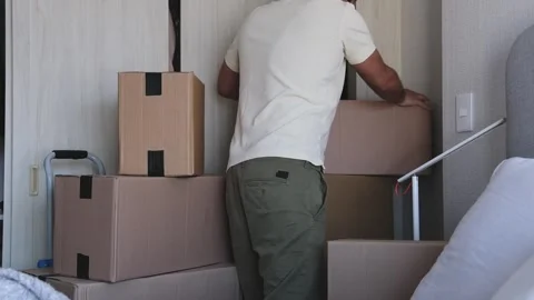 A man is standing in a room with boxes and clothes. New home concept. Stock Footage 315701017