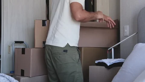 A man is standing in a room with boxes and clothes. New home concept. Stock Footage 315701050