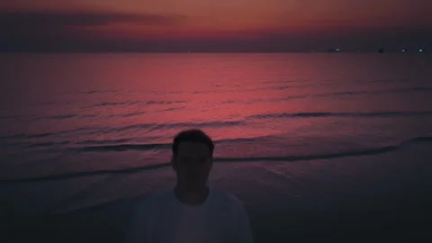 Man standing on sandy beach at sunset, operating drone to capture breathtaking Stock Footage 312741942