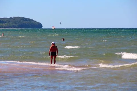 Man standing in sea water looking at green hill coastline. Stock Photos