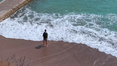 Man standing at the shoreline as waves crash around his feet Vídeo Stock 341295989